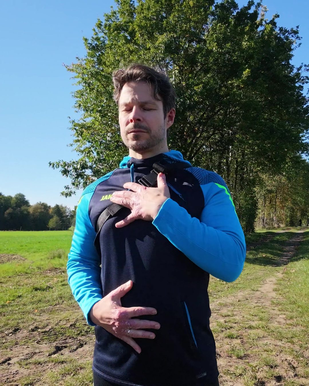 Dirk Gregor beim Qigong auf einem Feldweg, Augen geschlossen, eine Hand auf der Brust, eine auf dem Bauch